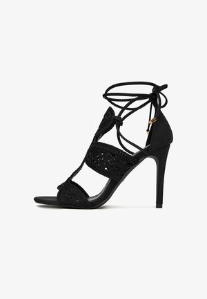 Sandalo nero con tacco alto, design ricamato intricato, punta aperta e cinturini alla caviglia regolabili con lacci. Texture liscia e tacco a punta.