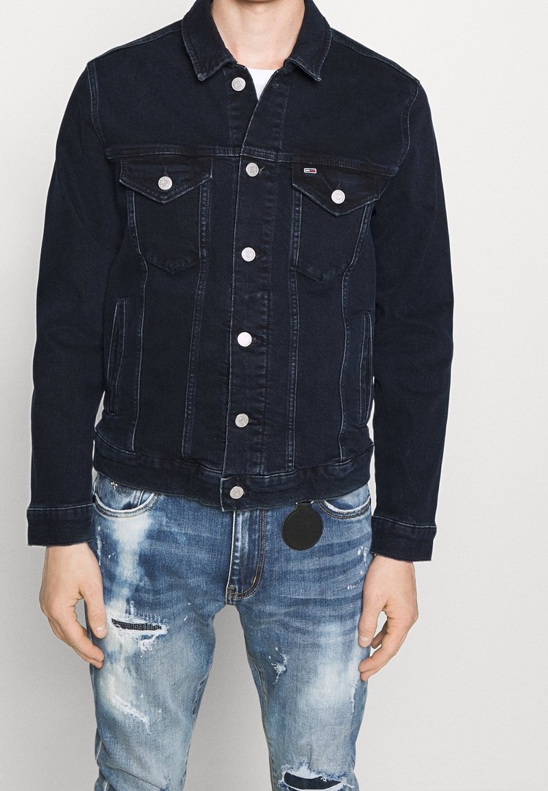 Tumma sininen denimpusero, jossa on napitettava etuosa, kaksi rintataskua, normaali kaulus ja pitkät hihat, jotka on kääräisty. Puseron alla on käytetyt siniset farkut.