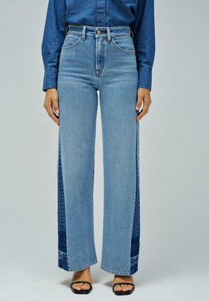 Jeans de tiro alto de color azul claro con piernas anchas, que presentan paneles laterales de denim azul oscuro en contraste y un dobladillo sin acabados en la parte inferior.