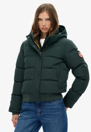 Polstret grøn jakke med hætte, frontlynlås og trykknaplukninger. Har sidelommer og ribbet kant. Stylet med blå jeans.