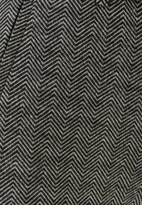 Textiel met een zwart-wit zigzagpatroon, met een gestructureerd, geweven ontwerp. De stof toont een vissengraatstijl.