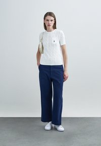 Λευκό κοντομάνικο πουλόβερ με πλέξη καλωδίου και εμπρόσθια τσέπη, συνδυασμένο με ναυτικό παντελόνι φαρδιάς γραμμής και λευκά αθλητικά. Μινιμαλιστικός σχεδιασμός, καθαρές γραμμές.