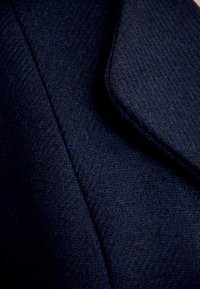 Granatowa tkanina w wzór jodełki, z wyraźnym kołnierzem. Tekstura wydaje się gładka i gęsta, z drobnymi włóknami.