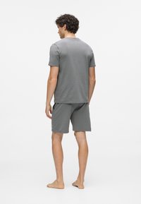 Hall hallist puuvillast lühikeste varrukatega särk ümmarguse kaelusega, sobitatud sobivate hallide lühikeste pükstega. Omaduseks on lõdvestunud istuvus ja minimaalne õmbluste detail.