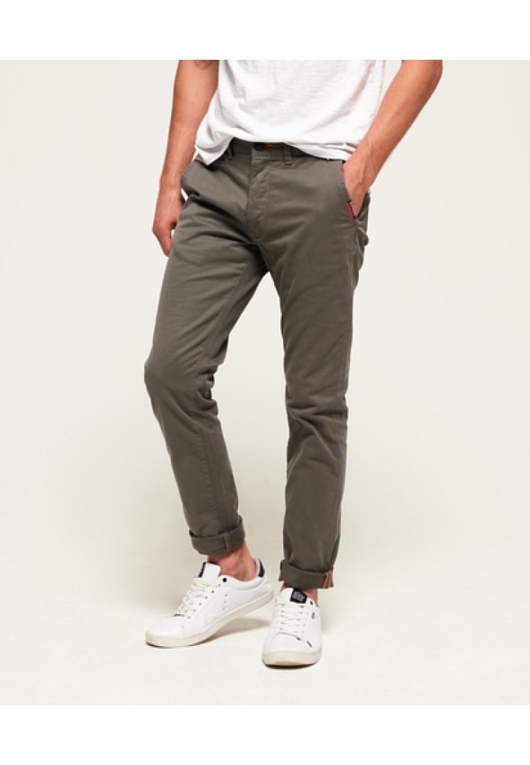 Chinos grigio scuro con vestibilità slim, orli arrotolati e dettagli rossi sulle tasche, abbinati a scarpe da ginnastica bianche. Tessuto di cotone morbido.