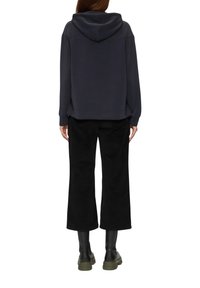 Donkergrijze hoodie met een capuchon, relaxte pasvorm, zijsplitten. Gecombineerd met zwarte wijde broek en zwarte kniehoge laarzen. Eenvoudig ontwerp.