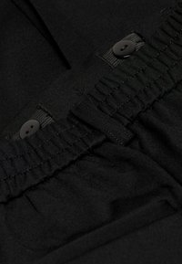 Schwarze Stoffhose mit Gummizug, verstellbarem Kordelzug, zwei Knöpfen und weicher Textur. Minimalistisches Design, ohne Muster.