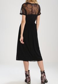 Svart klänning med en genomskinlig spetsöverdel, plisserad kjol och elastisk midja. Bärs med blomtryckta ankelskor.