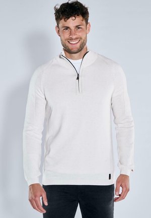 White long-sleeve pullover with a quarter-zip collar, ribbed cuffs, and a textured knit pattern. Styled with black jeans.