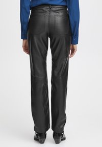 Zwarte leren broek met een aansluitende taille, op maat gemaakte achterzakken en een zachte textuur. Gecombineerd met zwarte schoenen en een blauw langarmshirt.