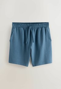 Shorts en tissu texturé bleu avec taille élastique et cordon de serrage ajustable, dotés de poches latérales sur un fond neutre.