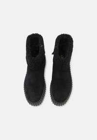 Botas de ante negras con un cuello texturizado y suave. Tienen una cremallera en el lateral y una suela de goma con patrones de agarre.