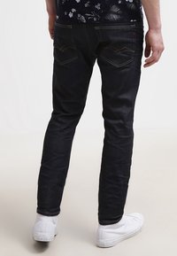 Mörk denimjeans med slim fit, med sömda bakfickor, subtila whiskeringar, och avslutade med vita sneakers.