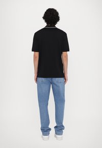 Cămașă polo neagră cu guler și manșete albe în contrast, asociată cu blugi din denim albastru deschis și adidași albi. Văzută din spate.