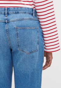 Blue denim jeans with a back pocket, high waist, and a slight fade. Accompanied by a long-sleeve red and white striped top at the waist.