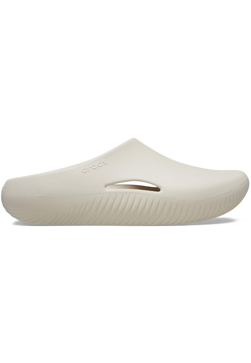 Beige Crocs Hausschuhe mit einer glatten, matten Oberfläche, die seitliche Aussparungen, eine dicke Sohle mit gerippter Textur und eine abgerundete Zehenpartie aufweisen.