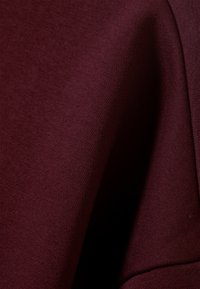 Tecido bordô mostrando uma superfície lisa e texturizada com uma vista aproximada, destacando um material macio e elástico sem padrões.