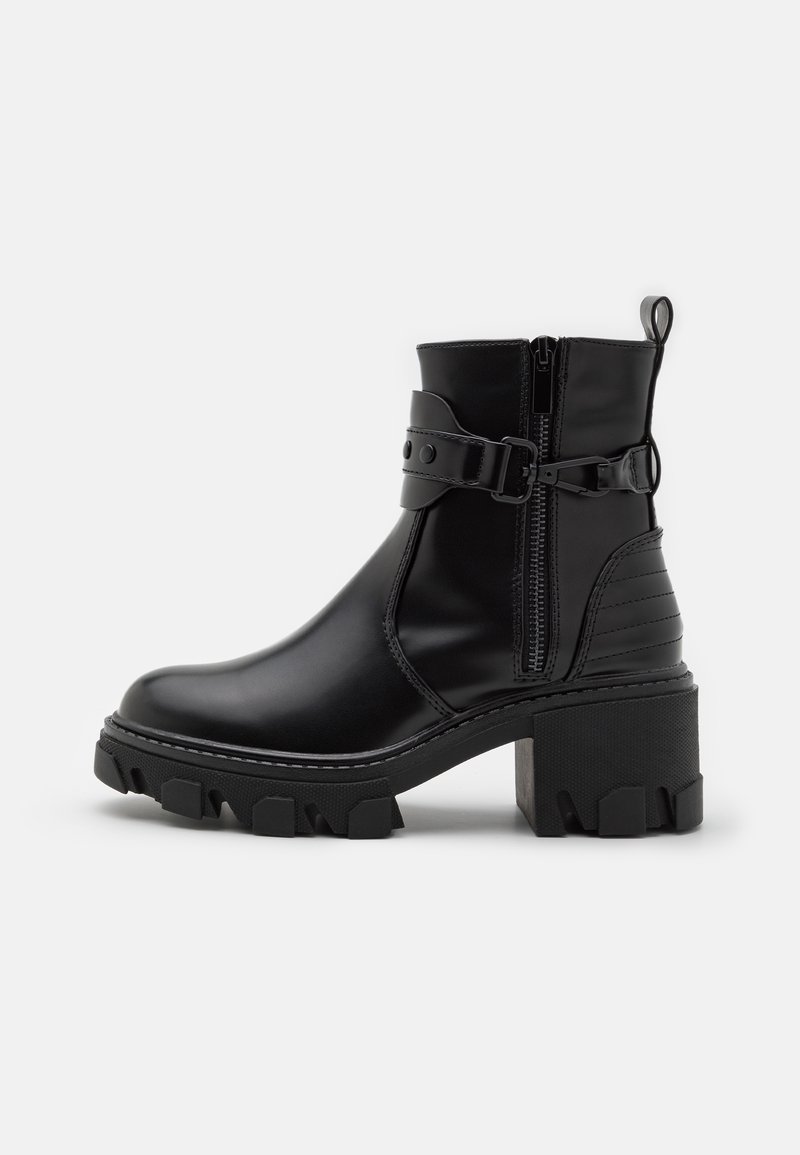 Bottine noire à semelle crantée épaisse, talon bloc, fermeture éclair latérale et sangle ajustable à boucle sur dessus en cuir lisse.
