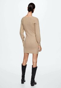 Robe tricotée beige à manches longues, à la silhouette ajustée et au dos décolleté, associée à de hautes bottes noires. Texture lisse, design décontracté.