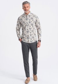 Blomstret langærmet skjorte i creme med blå og brune blomster; parret med grå slim-fit bukser og lysebrune sko.