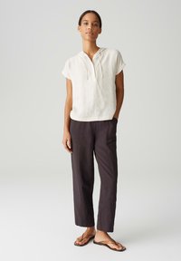 Maglietta a maniche corte di colore crema con cappuccio, abbinata a pantaloni scuri e larghi. Design minimalista e texture morbida.