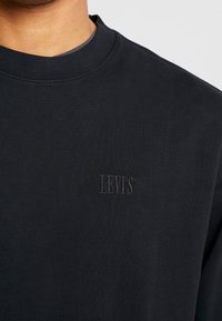 Sudadera negra de algodón con cuello redondo, con un logotipo de Levi's texturizado en relieve en el frontal. Textura suave y lisa, ajuste clásico.