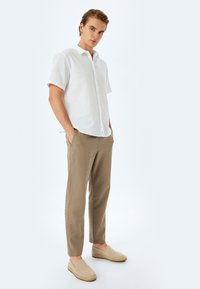 Witte korte mouwen button-up shirt, tan broek en geweven instap schoenen. De relaxte pasvorm en lichte stof creëren een casual uitstraling.