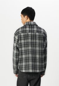 Gray plaid shirt jacket with a soft texture, featuring a collar and buttoned cuffs. The design includes alternating dark and light stripes.