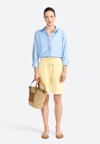 Light blue, long-sleeve shirt, yellow shorts with drawstring, tan flip-flops, and a woven basket bag with leather accents.