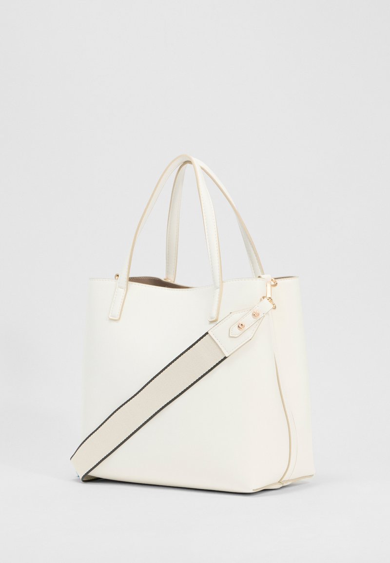 Sac fourre-tout en cuir couleur crème avec deux poignées et une bande large beige amovible avec des bords noirs sur fond blanc.