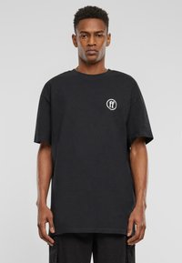 Black cotton t-shirt with a round neckline and short sleeves, featuring a white logo on the left chest and a relaxed fit.