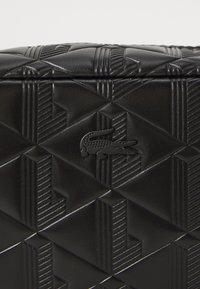Borsa in pelle nera con un motivo geometrico impresso, finitura testurizzata e un piccolo accento del logo nero sulla parte anteriore.