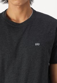 Svart bomull t-skjorte med rund hals, med en liten hvit 'GAP' logo på venstre brystområde. Enkelt design, myk tekstur.