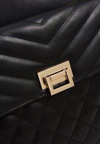 Czarna pikowana skórzana torebka z klapą, przeszywana wzorem jodełki, z złotym prostokątnym zapięciem na obrót.