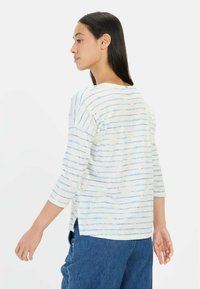 Lichte, gestreepte top in crème met blauwe horizontale lijnen, voorzien van driekwart mouwen, zijslitsen en een ontspannen pasvorm.