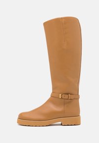 Botte en cuir haute et bronzée avec une texture lisse, un bout arrondi et un accent de boucle à la cheville. Semelle en caoutchouc épaisse pour une meilleure adhérence.