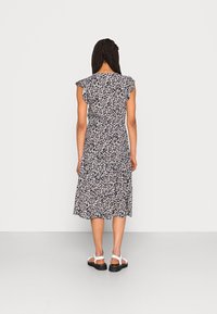 Blumenkleid in mittellanger Form mit gerafften Kappenärmeln, dunklem Hintergrund und einem Muster aus kleinen rosa und weißen Blumen. Trägt weiße Sandalen.