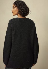 Overdimensioneret sort sweater lavet af blødt, fuzzy strikmateriale. Har en bred halsudskæring og lange ærmer, med en afslappet pasform og minimale sømme.