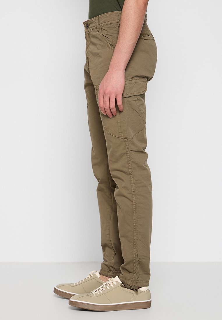 Pantalones cargo caqui de corte slim, con bolsillos laterales y una tela suave y texturizada. Combinados con zapatillas de color claro.