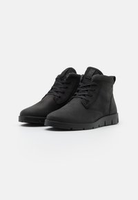 Botas de tobillo negras de ante con cierre de cordones, con punta redondeada y suela de goma con agarre texturizado, diseño minimalista.