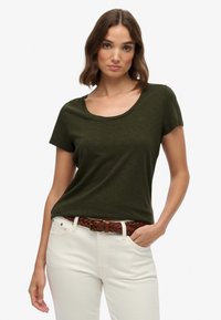Olivengrønt kortærmet t-shirt med rund halsudskæring og subtilt logodetail, parret med hvide bukser og et vævet brunt bælte.