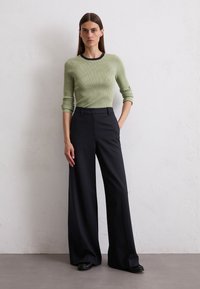 Rippengestricktes, langärmliges, hellgrünes Oberteil mit schwarzem Saum, kombiniert mit weitem, dunkelblauem Hosen. Die Textur ist glatt, mit klaren Linien und passgenauer Schnittführung.