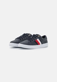 Sneakers in pelle blu navy con suole in gomma bianche, caratterizzati da occhielli dorati e un dettaglio a strisce intrecciate rosso, bianco e blu sul lato.