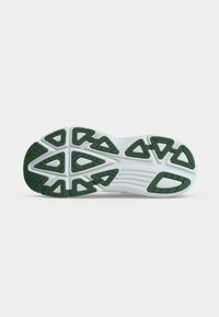 Semelle de chaussure avec base blanche et traction en caoutchouc vert en motifs triangulaires, affichant le nom de la marque Saucony sur un fond uni.
