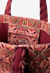Gewatteerde stoffen tas met bordeauxrode en roze bloemenpatroon, binnenvak met rits, magnetische druksluiting en twee gevoerde schouderbanden.