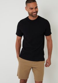 T-shirt noir à manches courtes avec une finition texturée, associé à un short beige. Le T-shirt a un col rond et une coupe décontractée.