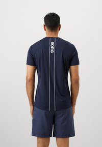 Άντρας με ναυτικού μπλε σορτς και ταιριαστό μπλουζάκι με κάθετες λευκές γραμμές και τη λέξη "BORG" στην πλάτη.