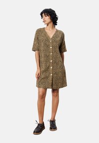 Robe à boutons à imprimé léopard marron et noir, avec des manches courtes et un col en V, associée à des chaussures à lacets noires.