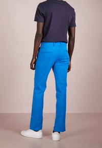 Blå bomullsbyxor med rak bendesign, sidofickor och bakfickor. Kombineras med en svart t-shirt med kort ärm och vita sneakers.