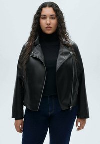Black leather jacket with a structured collar, zip closure, and two side pockets. Worn over a black turtleneck, paired with dark jeans.